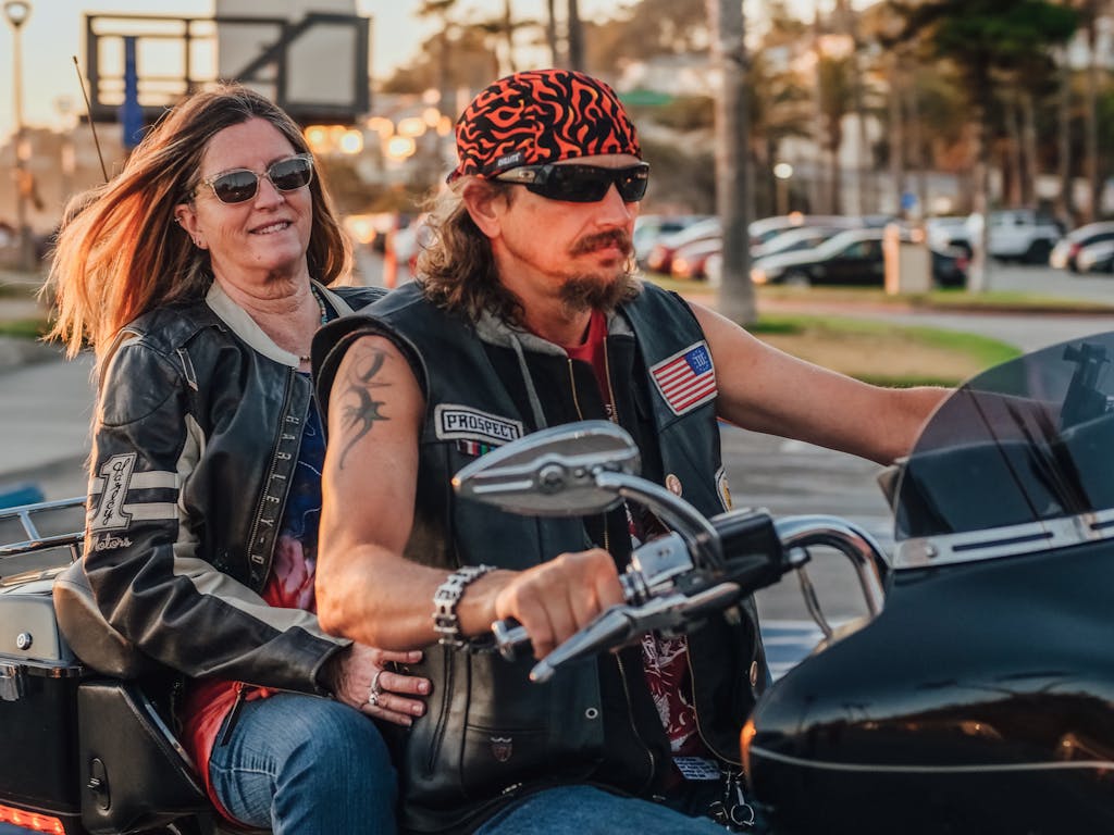 A couple on a motorcycle enjoying a scenic road trip at sunset wearing leather jackets and sunglasses.