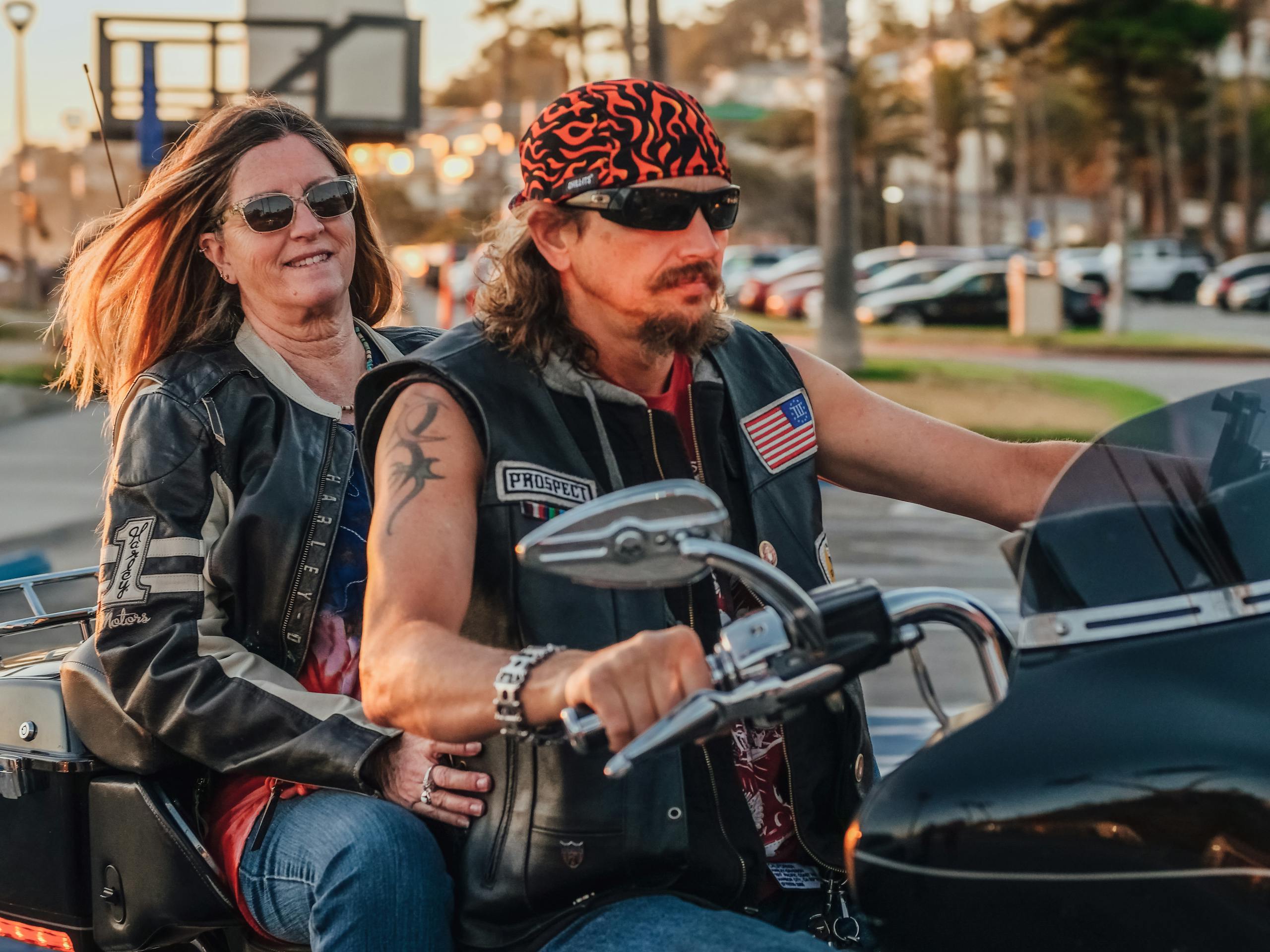 A couple on a motorcycle enjoying a scenic road trip at sunset wearing leather jackets and sunglasses.